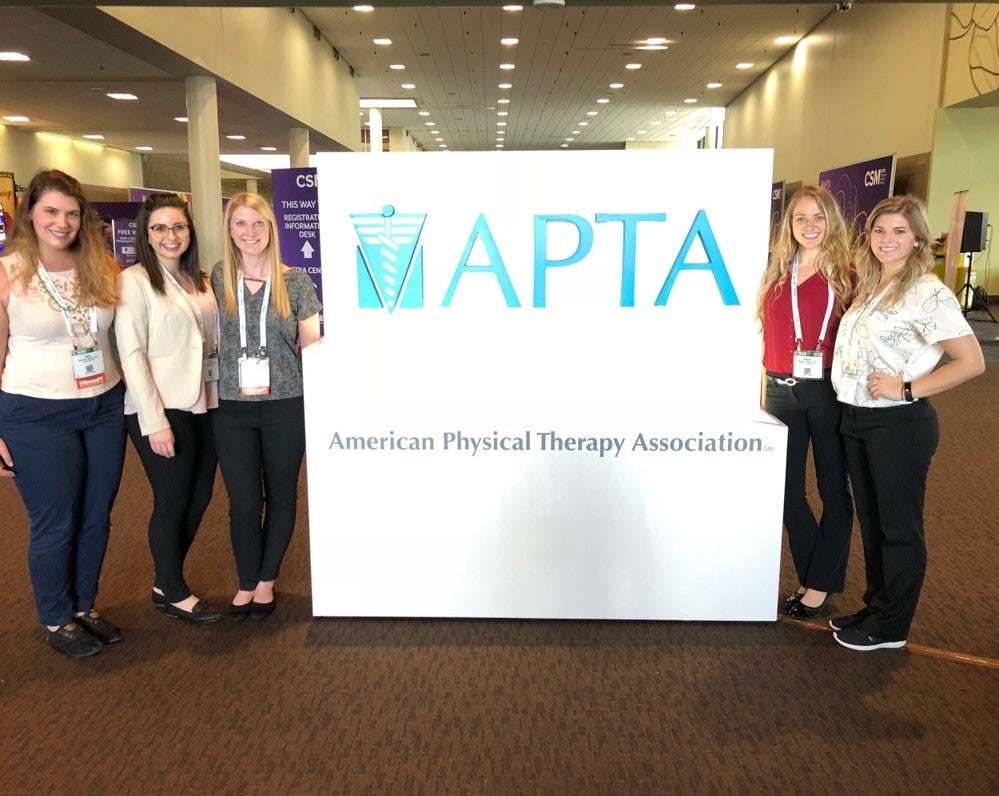 Five DPT Students standing next to a display sign for APTA