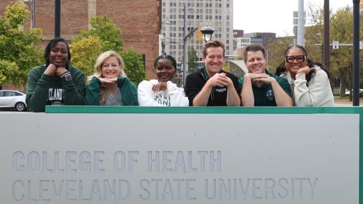 Academic coaches smiling standing behind College of Health sign